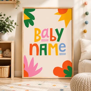 以下が含まれることがあります： カラフルで遊び心のある文字で「BABY NAME」と書かれた額入りのアートプリント。デザインには、クリーム色の背景に、緑、オレンジ、ピンク、黄色の花や太陽のような形が含まれています。プリントは木製のフレームに入っています。