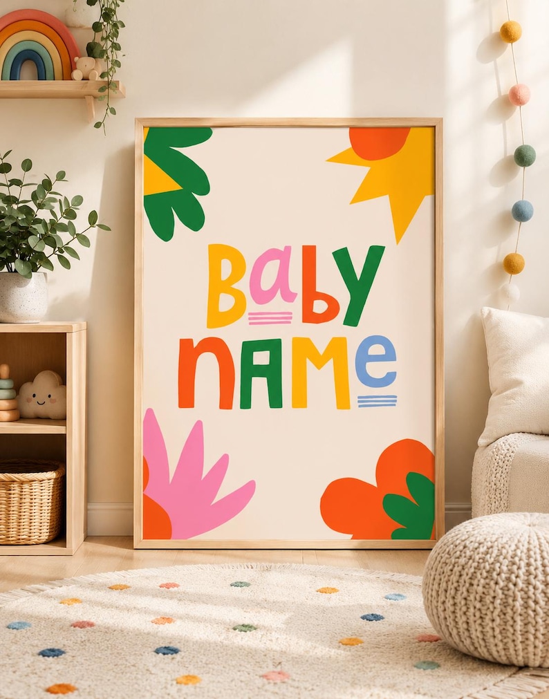 以下が含まれることがあります： カラフルで遊び心のある文字で「BABY NAME」と書かれた額入りのアートプリント。デザインには、クリーム色の背景に、緑、オレンジ、ピンク、黄色の花や太陽のような形が含まれています。プリントは木製のフレームに入っています。