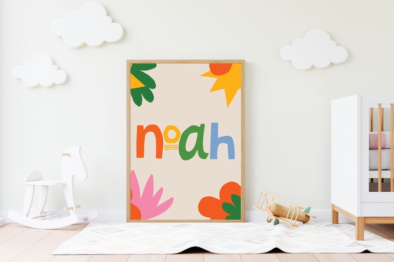 以下が含まれることがあります： カラフルで遊び心のある文字で「Noah」という名前が書かれた額入りのアートプリント。オレンジ、緑、黄色、ピンクの抽象的な花と太陽のデザインがベージュの背景に描かれています。プリントは子供部屋に飾られています。