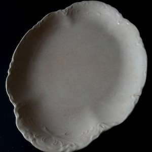 May include: Off-white, oval-shaped ceramic serving dish with a scalloped edge and embossed floral detailing. The dish has a matte finish and is set against a black background. A vintage-style piece for serving appetizers or desserts.