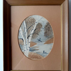 May include: Framed watercolor painting of a serene landscape featuring a birch tree, a body of water, and two ducks. The painting is set within an oval shape, framed by a brown wooden frame.