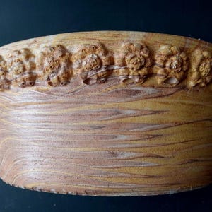 Puede incluir: Un cuenco redondo de cerámica hecho a mano con un aspecto veteado texturizado en tonos marrones y amarillos. El borde presenta una banda decorativa de pequeños diseños florales en relieve. El exterior del cuenco tiene una estética rústica y terrosa.