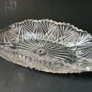 May include: A clear glass serving bowl with a decorative, cut-glass pattern. The bowl is oval shaped and has a scalloped edge.