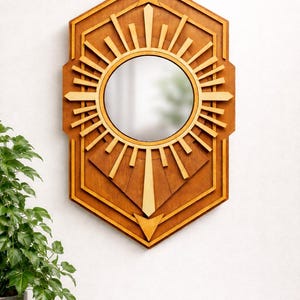 Pode incluir: Espelho de madeira com design de explosão solar com um centro de espelho redondo. O espelho é emoldurado por um design geométrico com um acabamento castanho claro. O espelho é montado numa parede branca, com uma planta verde num vaso cinzento no canto inferior esquerdo.