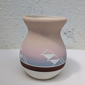 May include: A small, pink and white ceramic vase with a geometric design. The vase has a rounded base and a wide mouth.