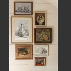 K&ouml;nnte beinhalten: Eine wei&szlig;e Wand mit einer Sammlung gerahmter Katzenillustrationen. Die Rahmen sind in verschiedenen Gr&ouml;&szlig;en und Farben, und die Illustrationen zeigen Katzen in verschiedenen Posen und Umgebungen. Einige der Katzen sind in Schwarzwei&szlig;, w&auml;hrend andere farbig sind.