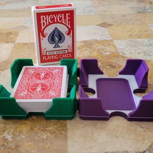 Puede incluir: Dos porta tarjetas, uno verde y otro morado, con una baraja de cartas Bicycle Elite Edition en el porta tarjetas verde.