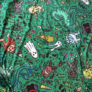 May include: Green fabric with a whimsical pattern of cartoon creatures, flowers, bones, and text. The design includes ghosts, a yeti, a frog, and the words "Stay Weird" and "My Goat."