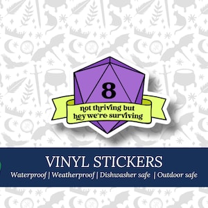 Puede incluir: Pegatina de vinilo morado y blanco con un dado morado de 8 caras con el número 8 en él. El dado está rodeado de una pancarta amarilla con el texto "not thriving but hey we're surviving".