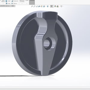 Op de afbeelding: Een grijze metalen knop met een puntige, driehoekige handgreep. De knop heeft een ronde basis en een gat in het midden.