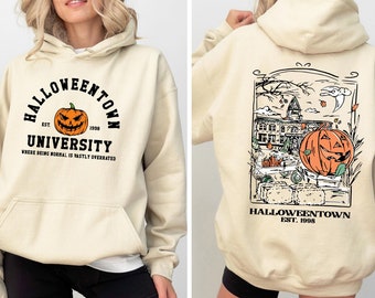 May include: Cream-colored Halloween-themed hoodie with a front graphic of a jack-o'-lantern and the text "Halloweentown University." The back features a detailed illustration of a pumpkin, buildings, and the text "Halloweentown Est. 1998."