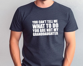 May include: Dark gray t-shirt with white text that reads: "YOU CAN'T TELL ME WHAT TO DO YOU ARE NOT MY GRANDDAUGHTER". The shirt has short sleeves and a crew neck.