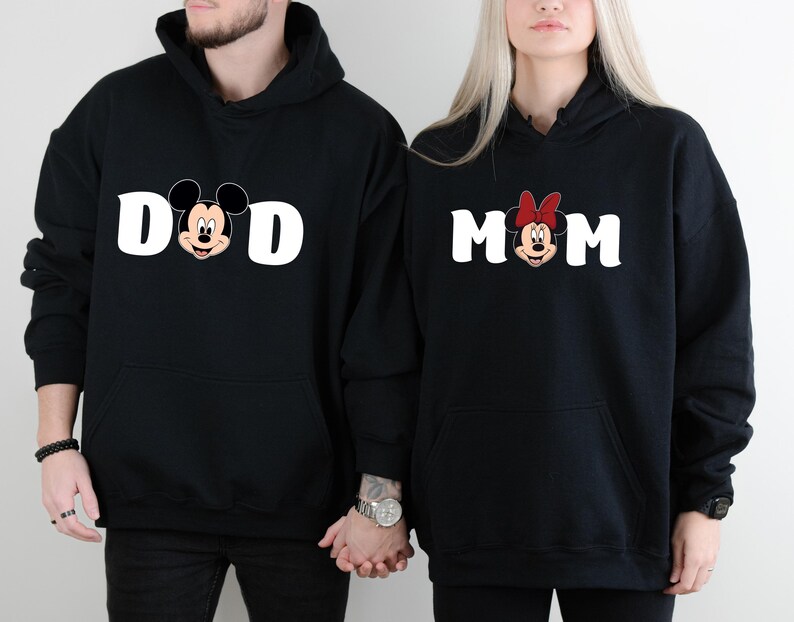 Pu&ograve; includere: Felpe con cappuccio nere con testo bianco e facce di personaggi dei cartoni animati. Una felpa dice "DAD" con Topolino, l'altra dice "MOM" con Minnie. Entrambe hanno una tasca frontale e un cappuccio.