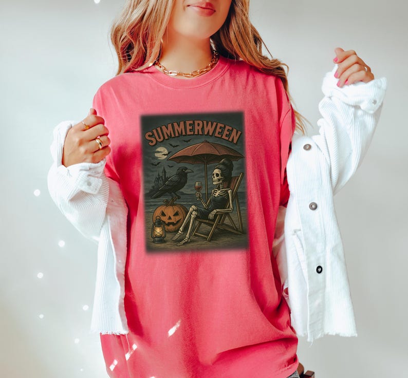 May include: A coral t-shirt with a graphic depicting a skeleton on a beach chair under an umbrella, holding a glass of wine. The image includes a raven, a jack-o'-lantern, and the word "SUMMERWEEN".