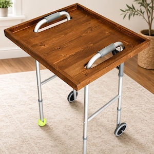 May include: A wooden serving tray table with a dark brown finish. It has a square top with cut-out handles and sits on a silver metal frame with wheels. The legs have tennis balls at the bottom.
