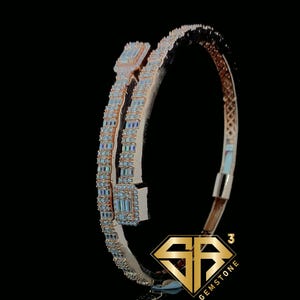 May include: Rose gold bracelet with rectangular and baguette-cut clear gemstones. The bracelet has a unique, open design with two parallel bands that meet at the top and bottom. The bracelet is set against a black background.