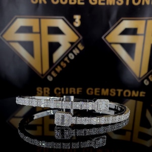 May include: A silver bangle bracelet with a double row of baguette-shaped diamonds. The bracelet is open and has a hinge closure.