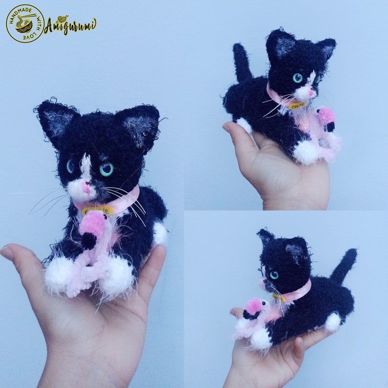 May include: Black and white crocheted cat amigurumi holding a pink flamingo amigurumi. The cat is wearing a pink ribbon around its neck. The amigurumi is handmade with love.