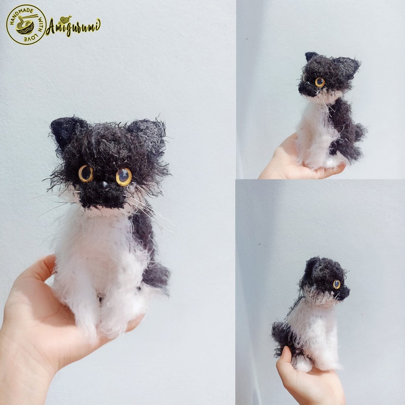May include: A black and white crocheted cat with yellow eyes. The cat is sitting on a hand. The cat is handmade with love.