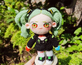 May include: A crocheted doll with green hair, black clothing, and red eyes. The doll is standing on a wooden base.