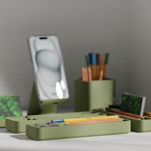 May include: A green desk organizer with multiple compartments for pens, pencils, and other office supplies. The organizer has a phone stand and a small tray for holding items.