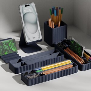 May include: A set of four dark blue desk organizers with various compartments. The organizers are made of a textured plastic and have a ribbed design. The organizers are filled with various office supplies, including pens, pencils, paper clips, and push pins.