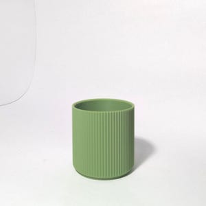 May include: A cylindrical, sage green container with vertical ribbed detailing. The container has a rounded base and a smooth interior. The product is set against a plain white background.