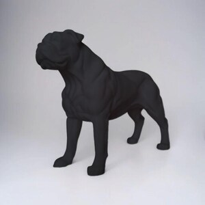 Könnte beinhalten: Eine schwarze Bulldoggen-Statue, die in einer stehenden Pose mit konzentriertem Blick dargestellt ist. Die Skulptur hat eine glatte, matte Oberfläche und steht vor einem schlichten weißen Hintergrund. Die muskulöse Form und die aufmerksame Haltung des Hundes sind deutlich erkennbar.