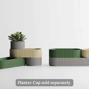 May include: A collection of modern planters in various colors, including green, gray, and tan. The planters have a ribbed texture and are arranged in a minimalist style. A succulent plant is in one of the planters. Text at the bottom reads "Planter Cup sold separately."
