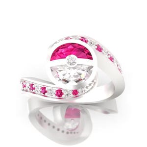 May include: A silver ring with a pink and white gemstone in the shape of a Pokeball. The ring is set with smaller pink and white gemstones.