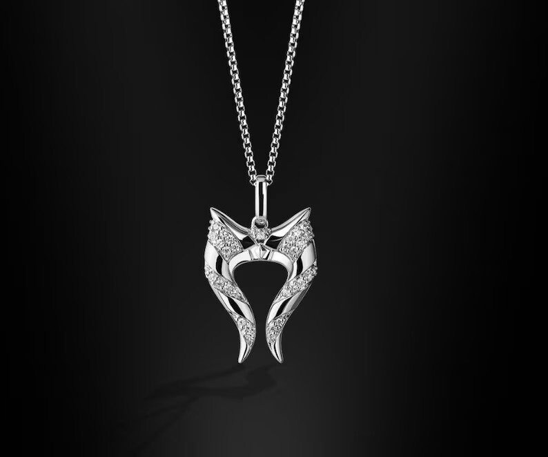 May include: A silver necklace with a pendant shaped like two horns with a row of small diamonds on each horn.