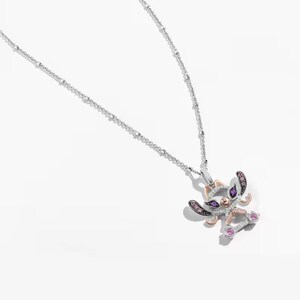 May include: A silver chain necklace with a charm of a cartoon alien character with pink, purple, and black accents. The charm is made of silver and has a rose gold accent.