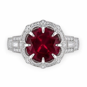 May include: A silver ring featuring a large, round, deep red center stone held by eight prongs. The setting is surrounded by a halo of small round diamonds and accented with baguette-cut diamonds on the band, all set in a polished silver metal.