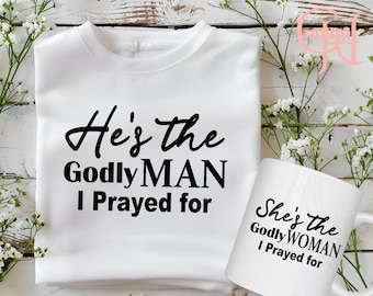 May include: Two white T-shirts with black text. One T-shirt says "He's the Godly MAN I Prayed for". The other T-shirt says "She's the Godly WOMAN I Prayed for".
