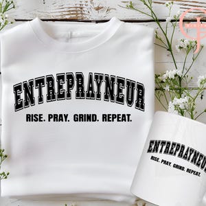 May include: White t-shirt with black text that reads "ENTREPRAYNEUR RISE. PRAY. GRIND. REPEAT."  A white mug with the same text is also shown.