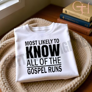 May include: A white t-shirt featuring the text "MOST LIKELY TO KNOW ALL OF THE GOSPEL RUNS" in black. The shirt is folded on a beige knitted surface, with books visible in the background.
