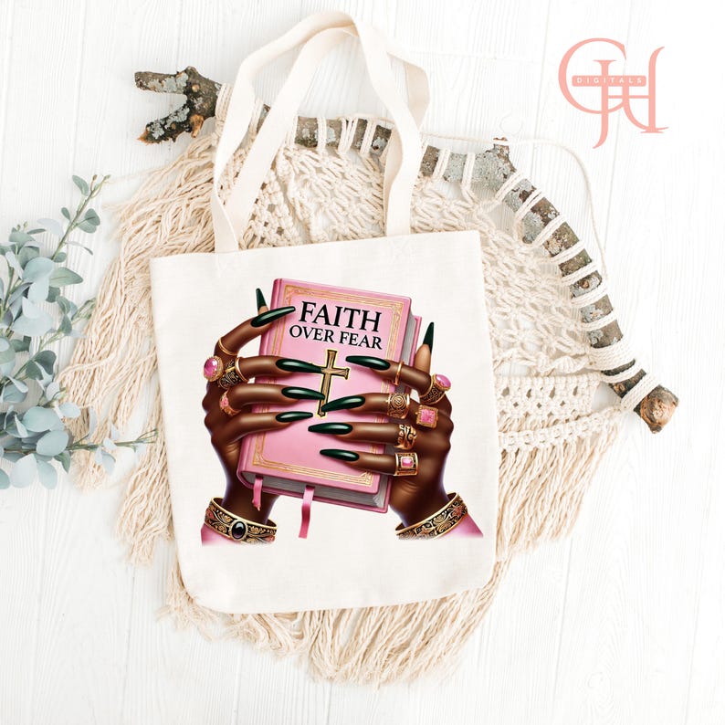 May include: White tote bag featuring a graphic of hands adorned with rings holding a pink book with the words "FAITH OVER FEAR" and a gold cross. The hands have long black fingernails. The bag has cream-colored handles.