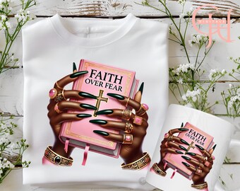 May include: White t-shirt and mug featuring a graphic of hands holding a pink book with the words "FAITH OVER FEAR" and a gold cross. The hands have long, dark green nails and are adorned with gold rings and bracelets. The design is set against a white background.