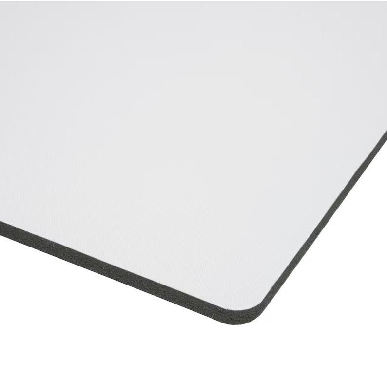 Op de afbeelding: Een wit rechthoekig product met een zwarte rand. De hoek van het product is afgerond. Het product is waarschijnlijk een whiteboard, een muismat of een vergelijkbaar artikel.