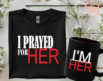 May include: Black t-shirt with white text that reads "I prayed for HER" in white and red. A black mug with white text that reads "I'M HER" in white and red.