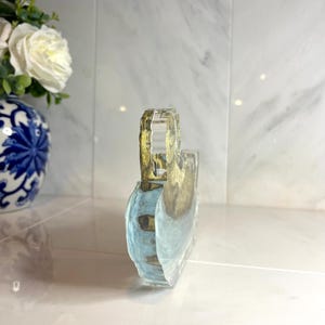 May include: A clear, rectangular decorative object with a handle. The object has a blue and gold design, possibly depicting a landscape or abstract art. The handle is a clear, faceted design.
