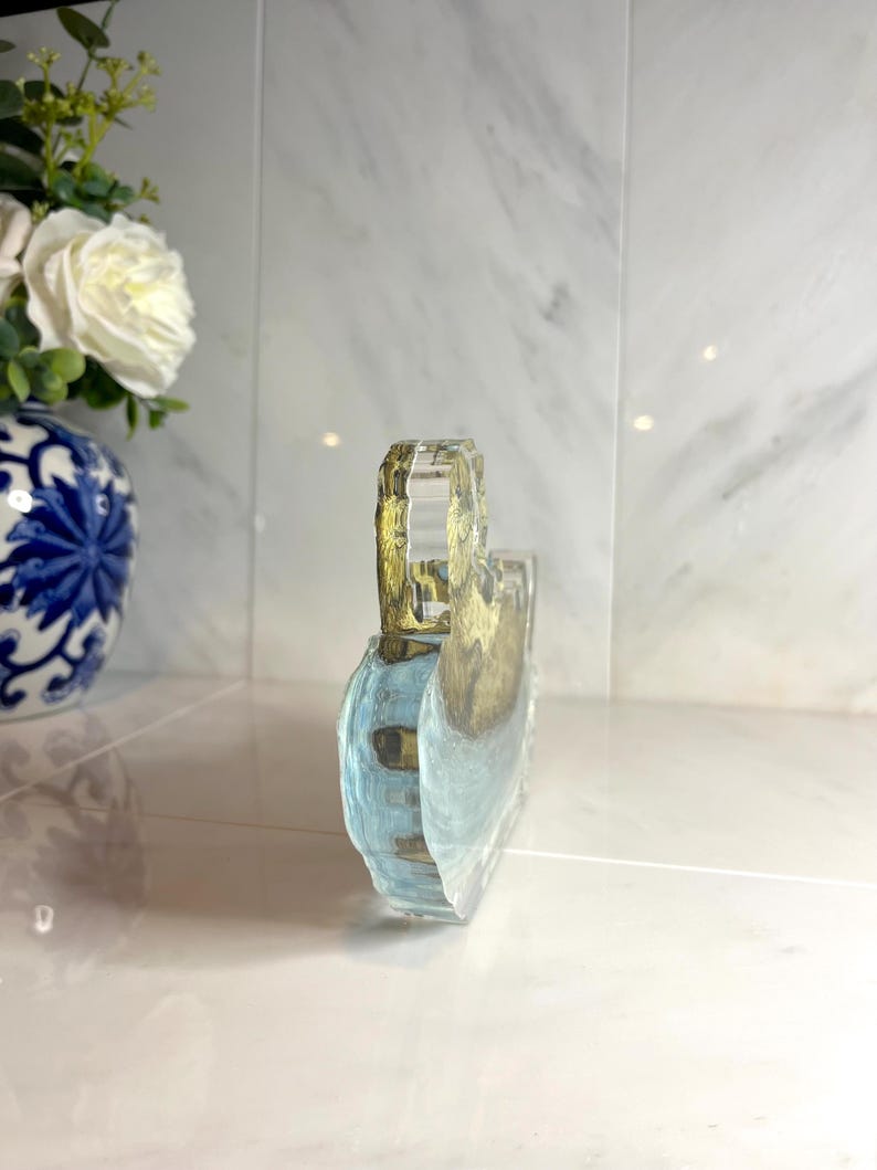 May include: A clear, rectangular decorative object with a handle. The object has a blue and gold design, possibly depicting a landscape or abstract art. The handle is a clear, faceted design.
