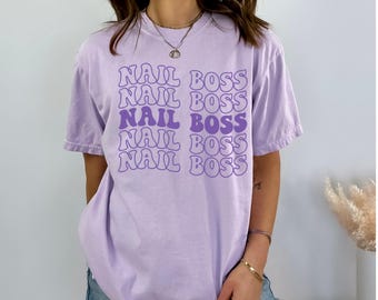 May include: A lavender t-shirt with the text "NAIL BOSS" repeated five times in a retro, purple font.