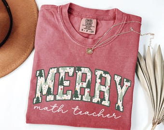 May include: Red t-shirt with a white graphic that says "Merry math teacher" with a Christmas tree pattern in the letters.