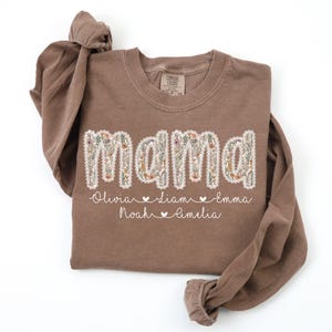 May include: A brown long-sleeved shirt with the word "mama" in a floral design. Below the word are the names Olivia, Liam, Emma, Noah, and Amelia, with hearts between the names.