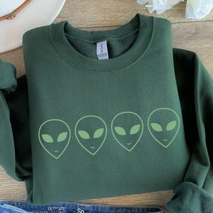 May include: A dark green sweatshirt with a row of five green alien faces printed on the front.