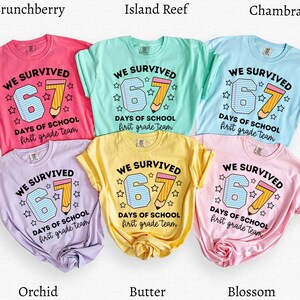 May include: A collection of six short-sleeved t-shirts in various colors, including pink, blue, yellow, and purple. Each shirt features the text "WE SURVIVED 67 DAYS OF SCHOOL first grade team" with a pencil graphic.