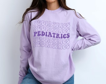 May include: A lavender long-sleeved t-shirt with the word "PEDIATRICS" repeated five times in a purple and white retro font.