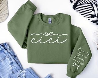 May include: A green sweatshirt with the word "cicci" written in white cursive on the front. The sleeves have the names "Everly", "Liam", "Lucas", and "Violet" written in white cursive.