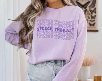 May include: A lavender long-sleeved shirt with the text "Speech Therapy" repeated five times in a purple retro font.